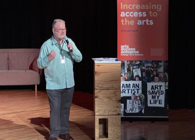 Richard Benge on stage, speaking to participants  